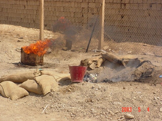 Burning waste in a cut-down drum behind sandbags, May 2003.